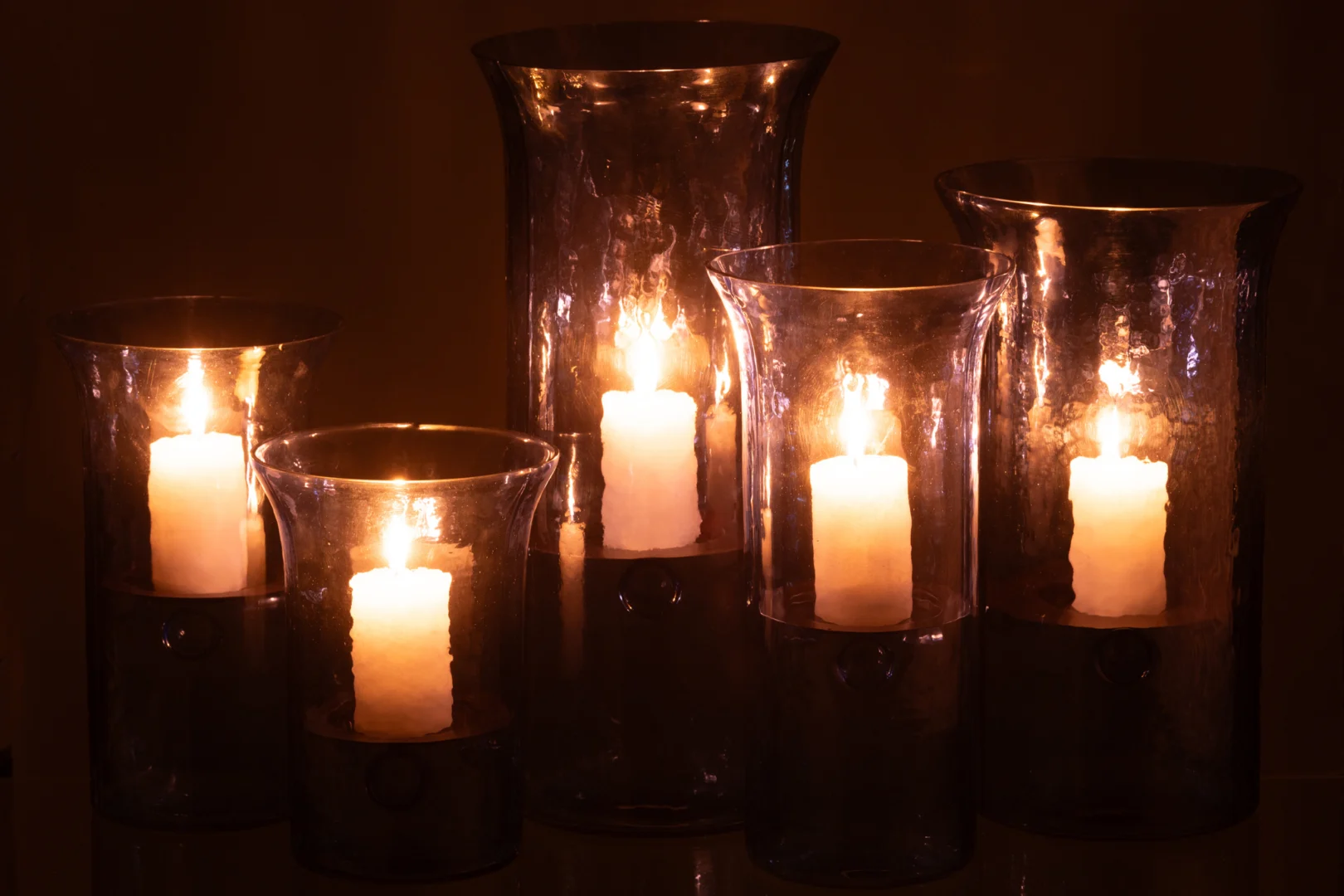 Vijf verlichte Orkaan Tarifa Smal Glas Blauw Extra Groot kaarsenhouders werpen een warme gloed in het donker en creëren zo een gezellige en vredige sfeer.