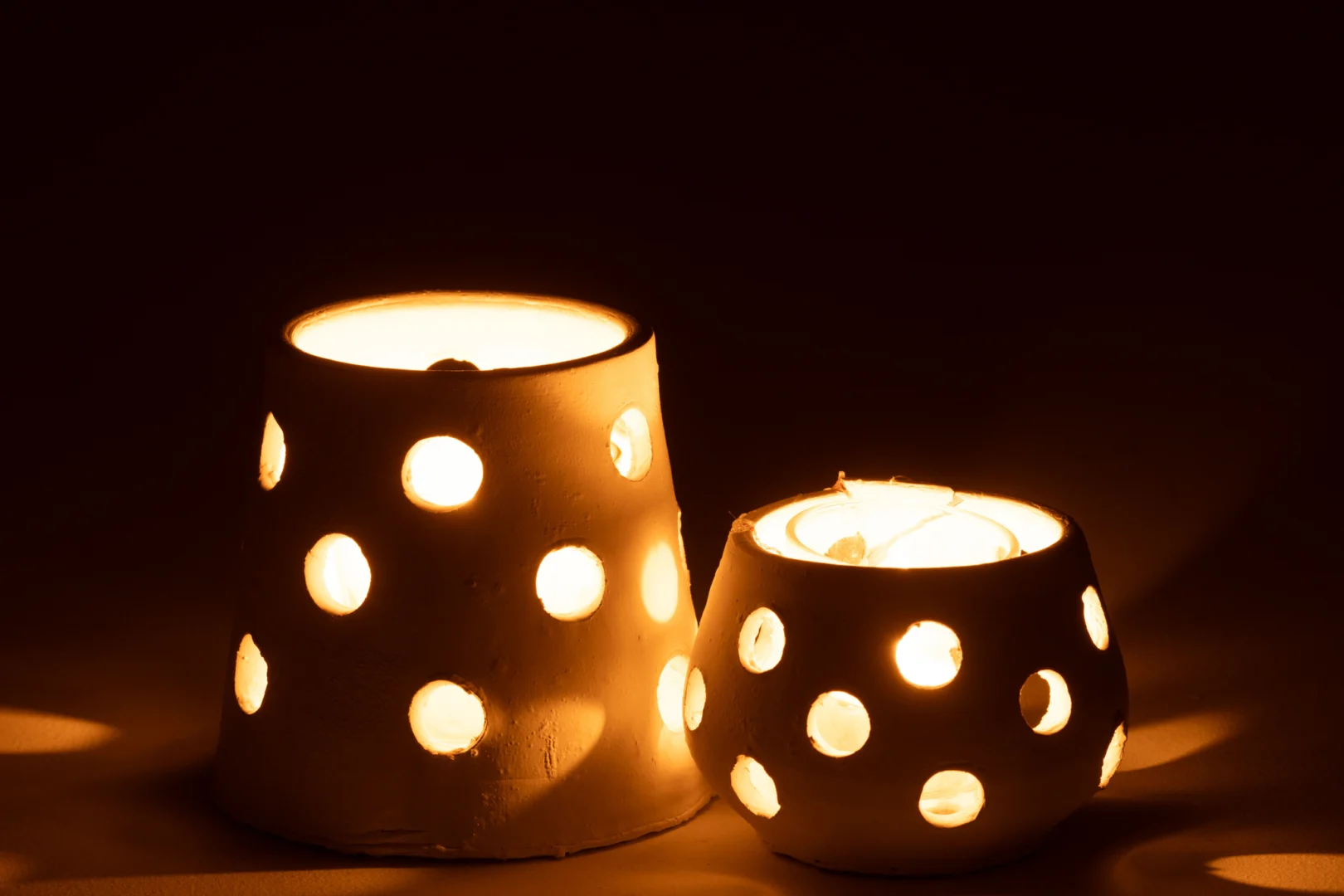 Theelichthouder Ibiza Klei/Glas Wit Smal werpt een warme gloed in het donker, met zijn ronde uitsparingen die zacht licht en zachte schaduwen creëren.