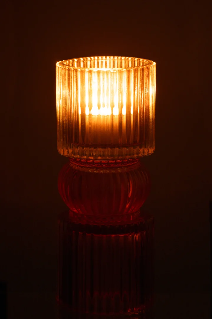 De Kaarsenhouder Jazzy Glas Mix heeft een brandende kaars in een geribbelde glazen houder, die warm oplicht in het donker om zacht licht te werpen en een gezellige, uitnodigende sfeer te creëren.