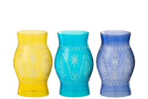 De Orkaan Tarifa Glas Mix Set van 3 - Kaarsenhouders heeft drie glazen kandelaars in geel, groenblauw en blauw met wit geëtste bloem- en bladmotieven, naast elkaar op een witte achtergrond.