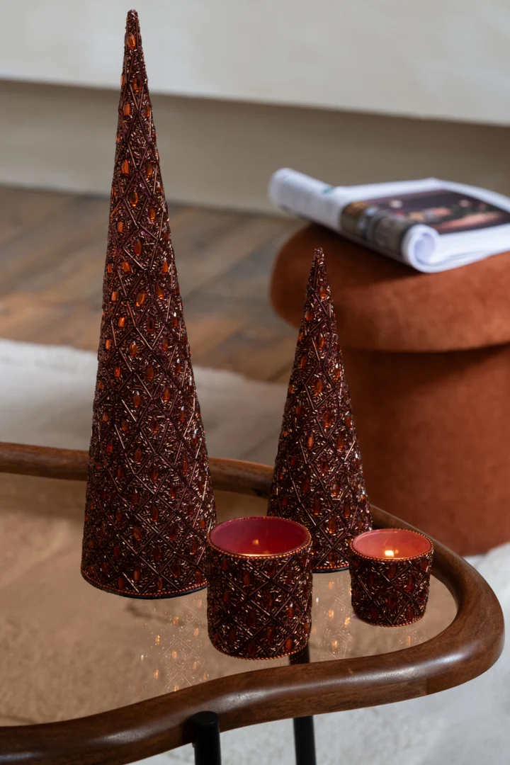 Twee decoratieve kegelbomen en twee kleine Theelichthouder Glas Kralen Donkerbruin Roestbruin Klein staan op een glazen salontafel. Op de achtergrond zie je een opgerold tijdschrift en een oranje voetenbankje.