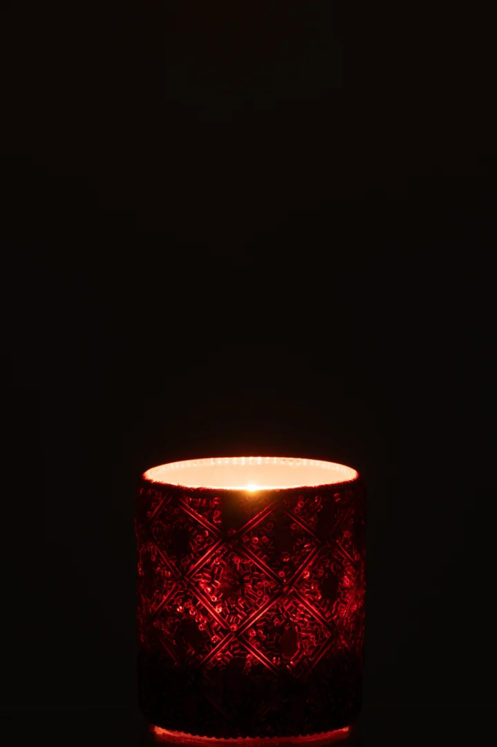 Een enkele brandende kaars gloeit zacht in de Theelichthouder Glas Kralen Donkerbruin Roestbruin Groot, de decoratieve bruine glazen houder glinstert tegen een donkere achtergrond.