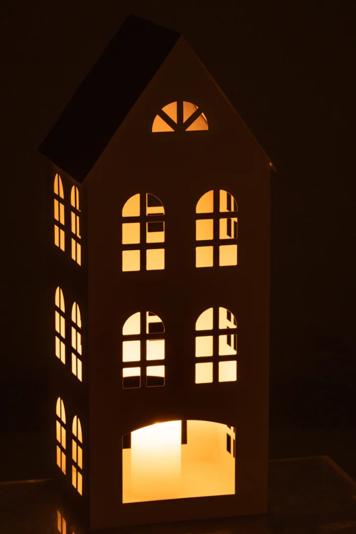 Het Kaarsenhouder Huis Psi IJzer Wit is een oplichtend miniatuurhuis met boogramen en een puntdak, van binnenuit verlicht tegen een donkere achtergrond.
