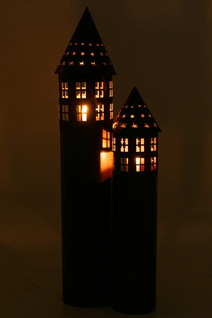 Twee hoge, cilindervormige lantaarns van Kaarsenhouder Ster IJzer Roestbruin in de vorm van huisjes met sterretjes stralen een warme gloed uit in het donker en verlichten hun ramen en perforaties.