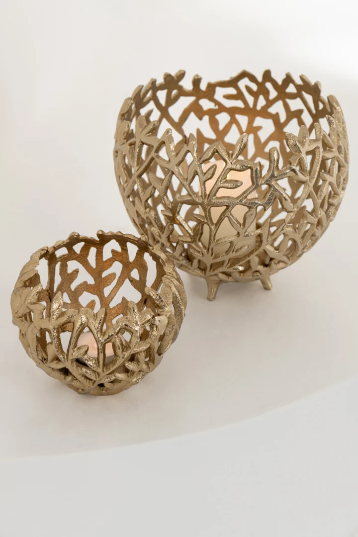 De Kaarsenhouder Blad Aluminium Goudkleurig Klein, een goudkleurige metalen kaarsenhouder met een ingewikkeld bladpatroon voor waxinelichtjes, staat op een licht oppervlak naast zijn grotere tegenhanger.