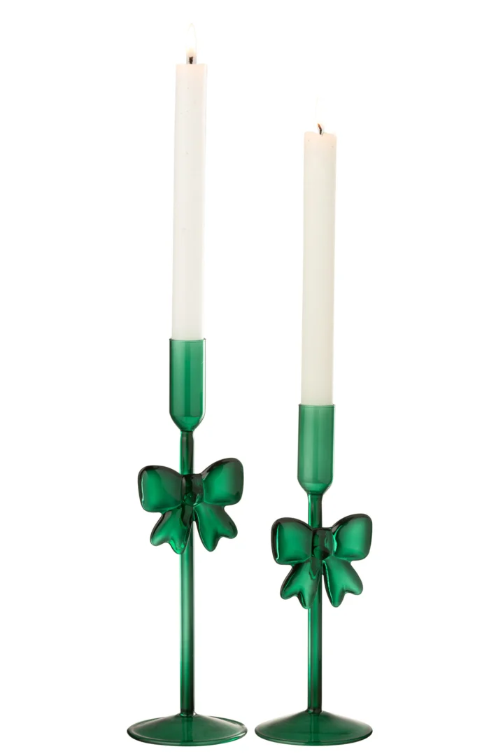 De Kaarsenhouder Glas Donkergroen Set van 2 bestaat uit twee glanzend groene glazen kandelaars van iets verschillende hoogtes, elk met een strikdecoratie en met hoge, brandende witte kaarsen.