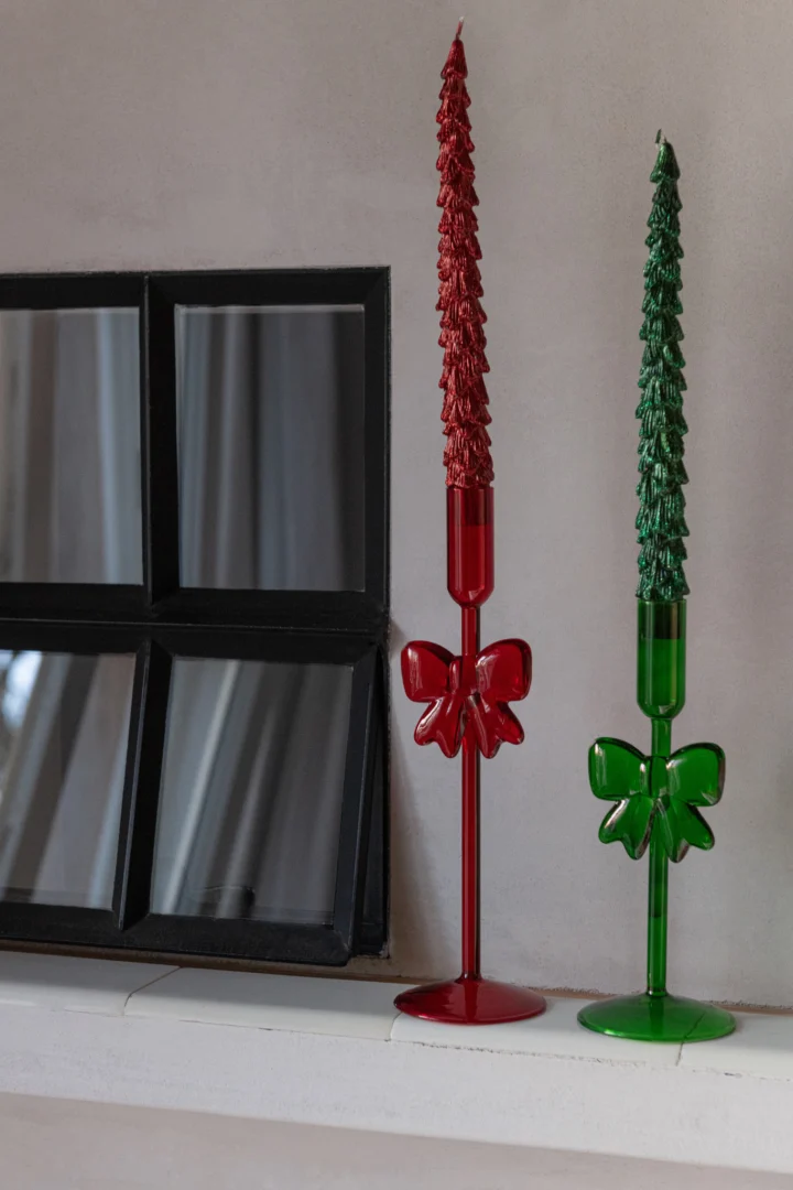 Twee Kaarsenhouder Glas Donkergroen (Set van 2) staan op een witte plank naast een kleine, vierkante spiegel met zwarte lijst.