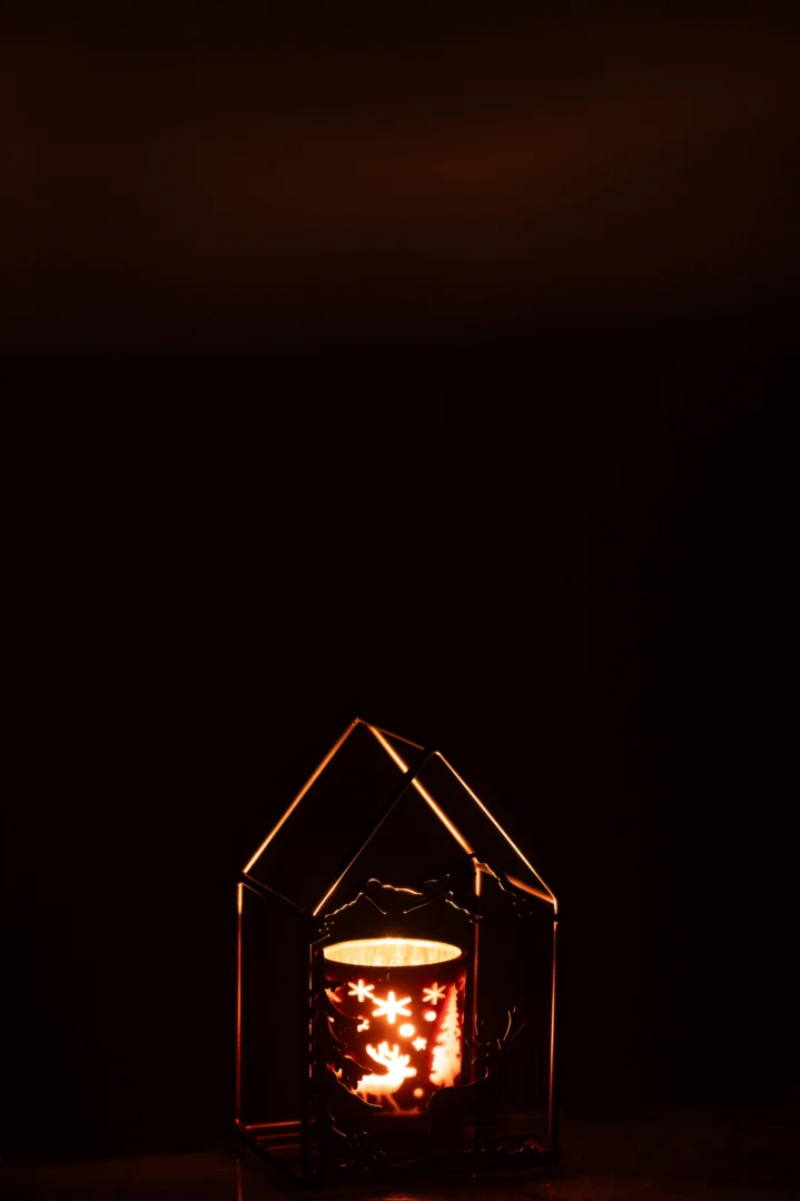 Een gloeiende kaars verlicht de Theelichthouder Huis Glas IJzer Roestbruin Bruin, waarvan de ster- en sneeuwvlokpatronen een warm, knus licht werpen tegen een donkere achtergrond.