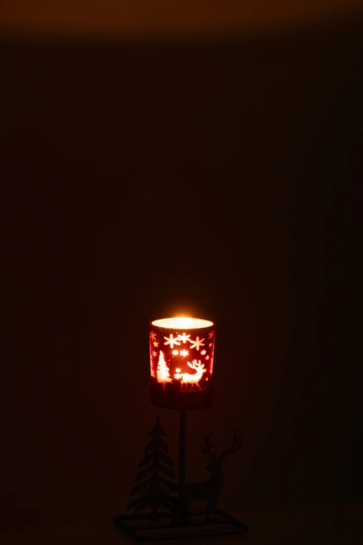 De Theelichthouder Winter IJzer Roestbruin Bruin is een bruine ijzeren kandelaar met sneeuwvlok-, rendier- en boommotieven. Als hij brandt, werpt hij een warme gloed die de patronen benadrukt en een gezellige wintersfeer creëert.