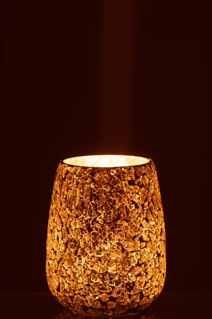 De Kaarsenhouder Gebarsten Glas Goudkleurig werpt een warme oranje gloed in een donkere kamer. Het gebarsten glas en de gouden afwerking accentueren het gestructureerde, mozaïekachtige oppervlak.