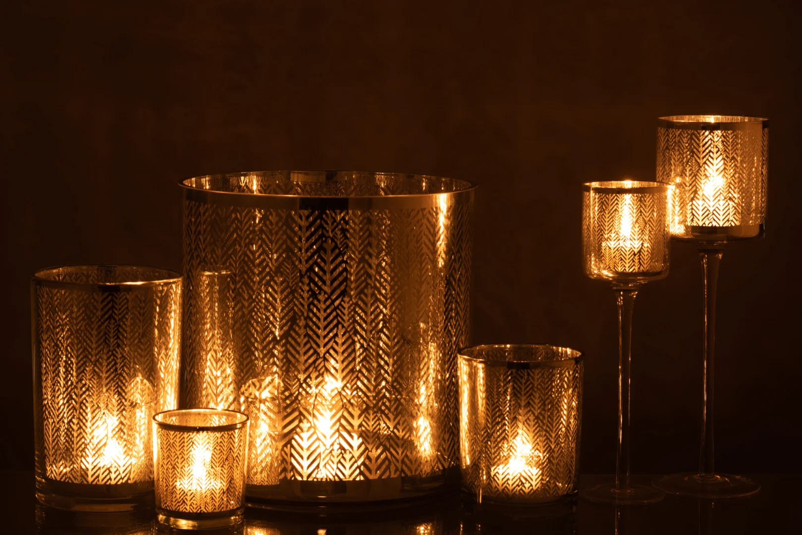 De Kaarsenhouder Glas Graanmotief Zilver Goud Grijs Set 3 bestaat uit drie glazen kandelaars in zilver, goud en grijs met een graanmotief. Als ze branden, creëren ze een gezellige en elegante sfeer met hun warme gloed en gevarieerde afmetingen.