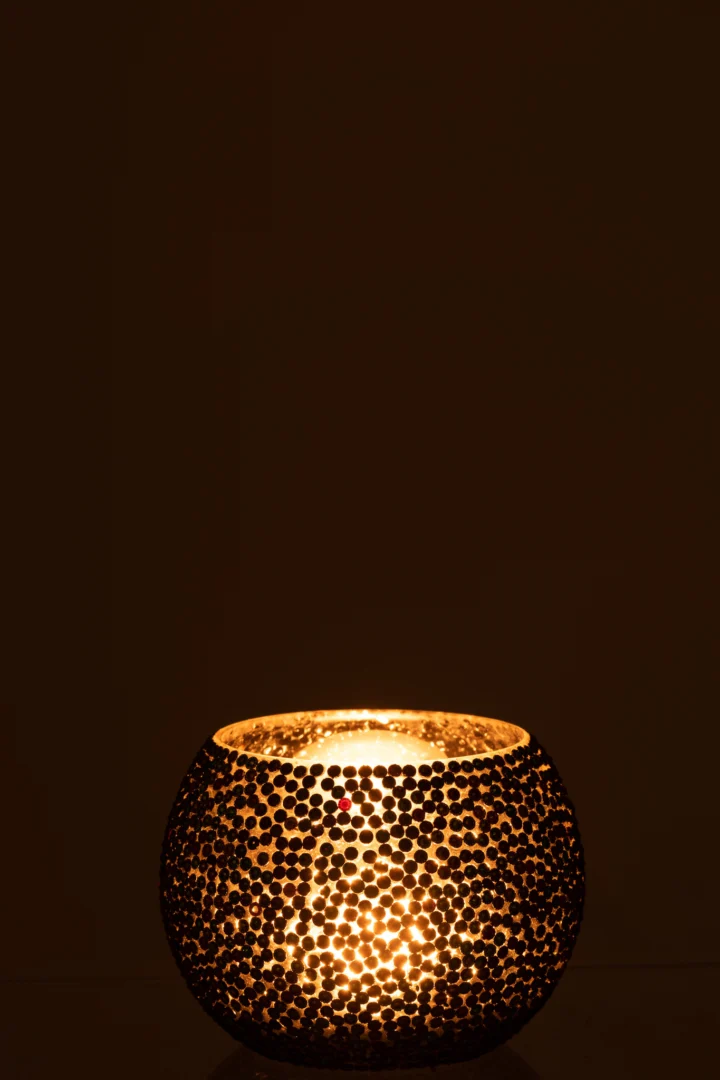 De Theelichthouder Diamant Glas Blauw Groen Middel werpt een warm, stralend licht door het facetgeslepen glas en creëert een gezellige sfeer tegen een donkere achtergrond.