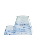 Twee Orkaan Golven Glas Blauw kaarsenhouders, gemaakt van helder glas met wervelende blauwe en witte motieven die doen denken aan aquarelstreken, worden weergegeven op een effen witte achtergrond. De ene houder is groter dan de andere.