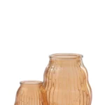 De Kaarsenhouder Orkaan Glas Gestreept Oranje Medium, een geribbelde, doorschijnende amberkleurige glazen vaas met een smalle opening en een ronde vorm, staat op een witte achtergrond naast een kleinere vaas ervoor.