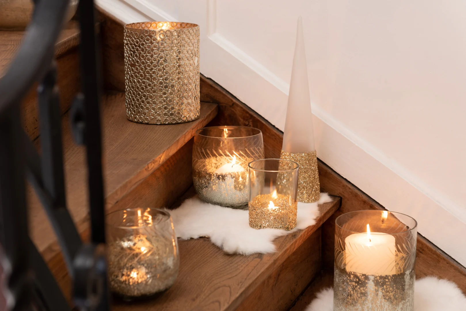 Verschillende Kaarsenhouder Orkaan Cirkels Glas Zilver kandelaars met zilveren accenten en brandende kaarsen staan op een houten trap, met wit imitatiebont eronder voor extra decoratie.