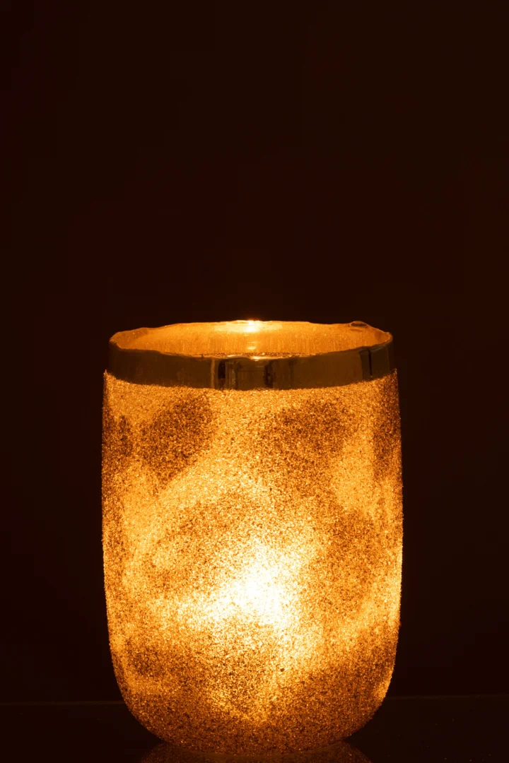 De Theelichthouder Frosty Ronde Glas Zilver Extra groot is een gloeiend gouden kandelaar met een gestructureerd, mat oppervlak en metalen rand, die warm licht uitstraalt tegen een donkere achtergrond.