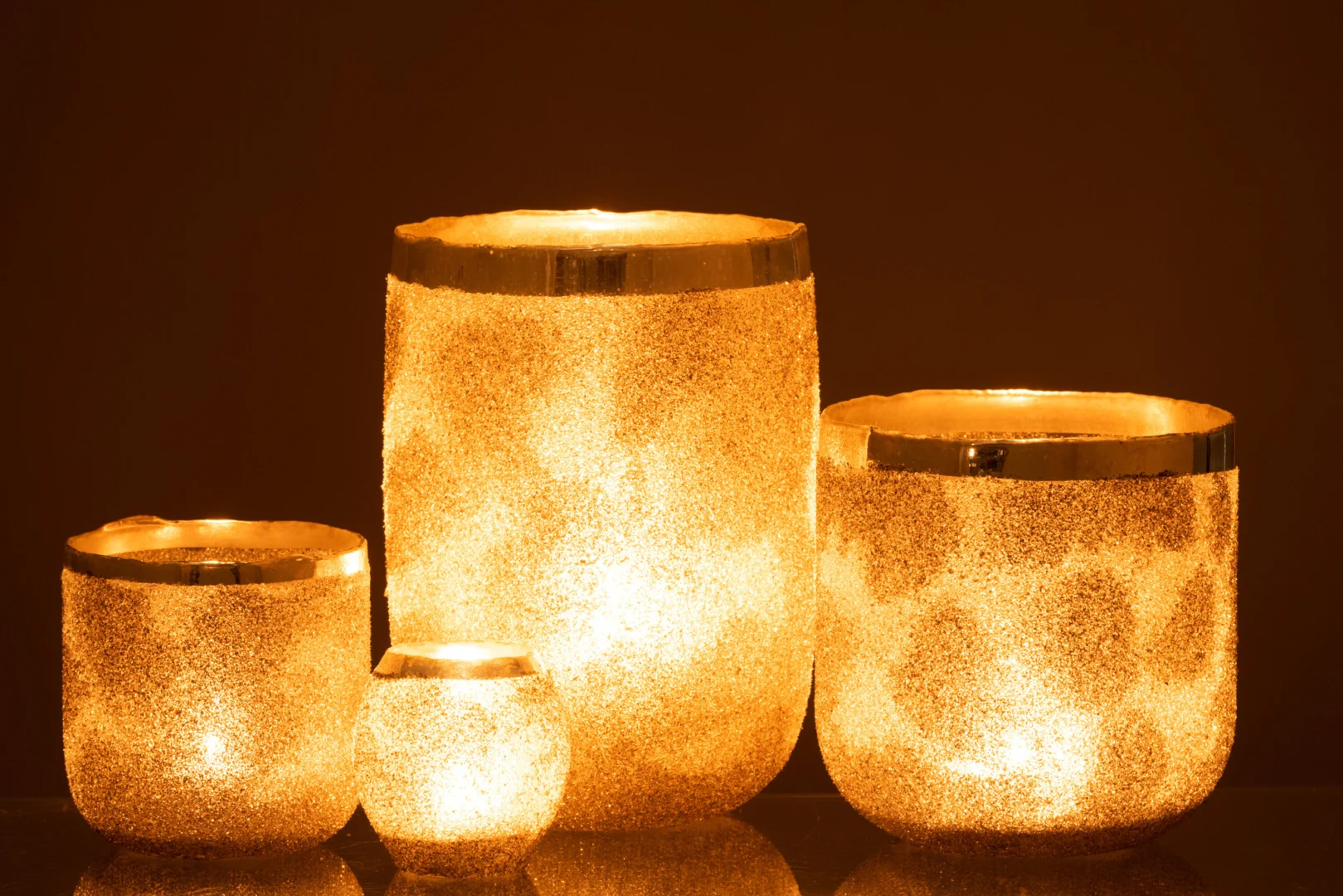 De Theelichthouder Frosty Ronde Glas Zilver Extra groot gloeit warm tegen een donkere achtergrond en creëert een gezellige en elegante sfeer met zijn glinsterende zilveren ontwerp.