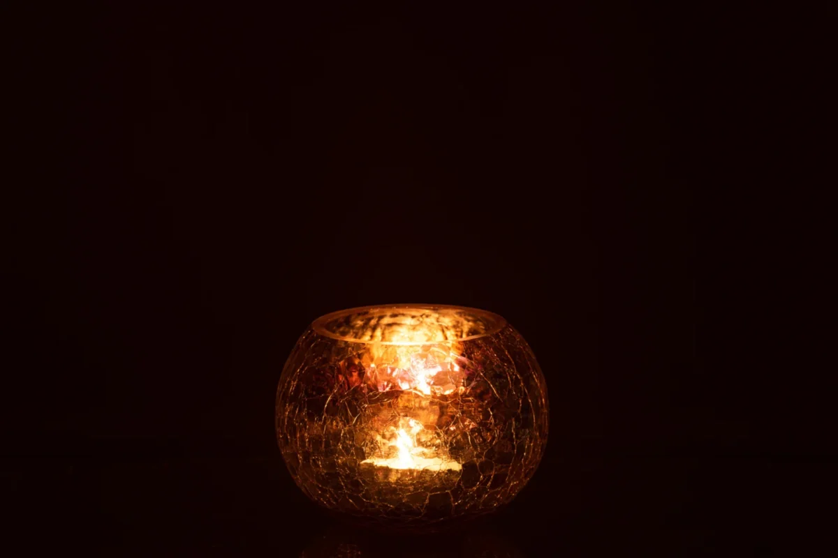 De Kaarsenhouder Orkaan Lichtbal Craquelure Glas Paars Medium gloeit warm in een donkere ruimte, werpt zacht gouden licht en subtiele reflecties op het oppervlak eronder.