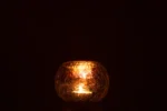 De Kaarsenhouder Orkaan Lichtbal Craquelure Glas Paars Medium gloeit warm in een donkere ruimte, werpt zacht gouden licht en subtiele reflecties op het oppervlak eronder.