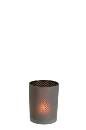 De Kaarsenhouder Orkaan Chevron Glas Bruin Klein is een brandende kaars in een decoratieve, matbruine glazen houder met een subtiel chevronpatroon, die warm oplicht tegen een effen witte achtergrond.