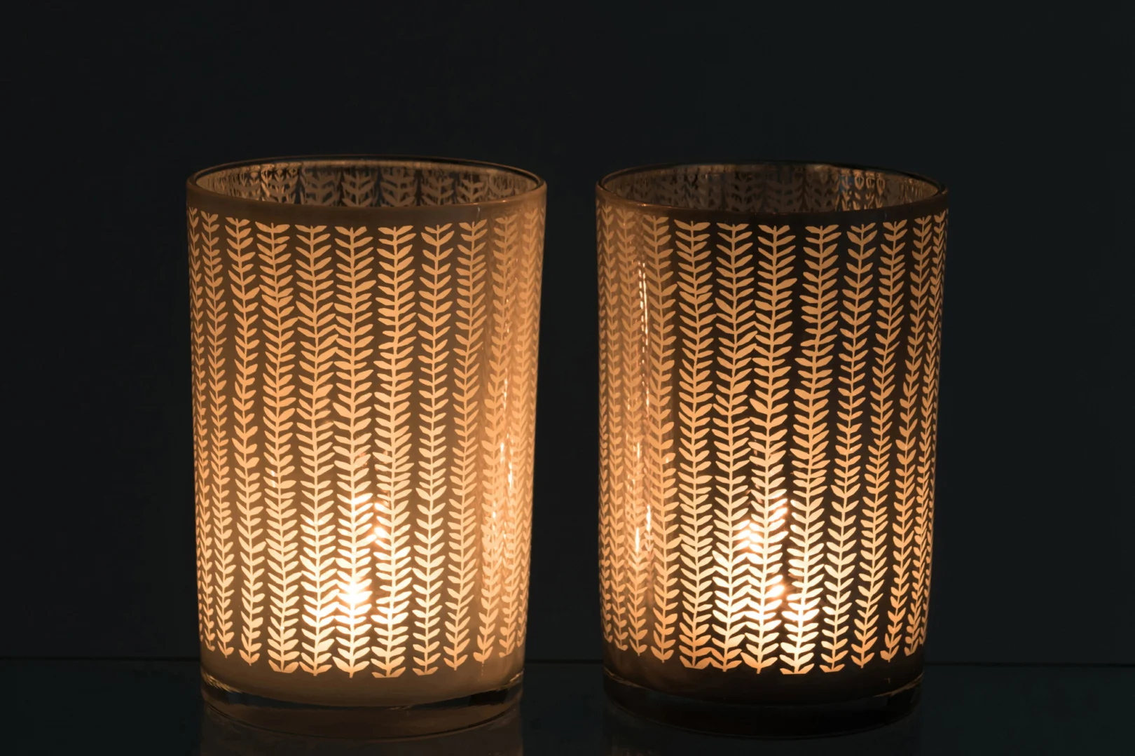 De Kaarsenhouder Orkaan Sarah Glas Wit Blauw Groot Set 2 heeft twee glazen kandelaars met opvallende verticale patronen die warm oplichten in het donker, waardoor er prachtige licht- en schaduweffecten ontstaan als de kaarsen erin branden.