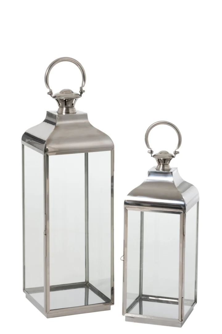 De Lantaarn Evi Ring Metaal Glas Zilver Set 2 heeft twee rechthoekige lantaarns van zilverkleurig metaal en glas van verschillende hoogtes, elk met een rond handvat bovenop, tegen een witte achtergrond.
