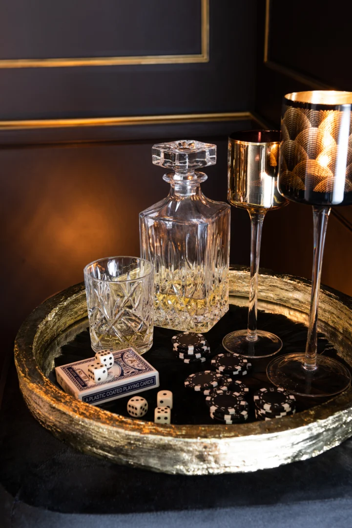 Een set van twee kleine zwart met gouden Gatsby glazen kandelaars staat op een dienblad met een karaf, glazen, metalen bekers, pokerchips, kaarten en dobbelstenen tegen een elegante donkere achtergrond.