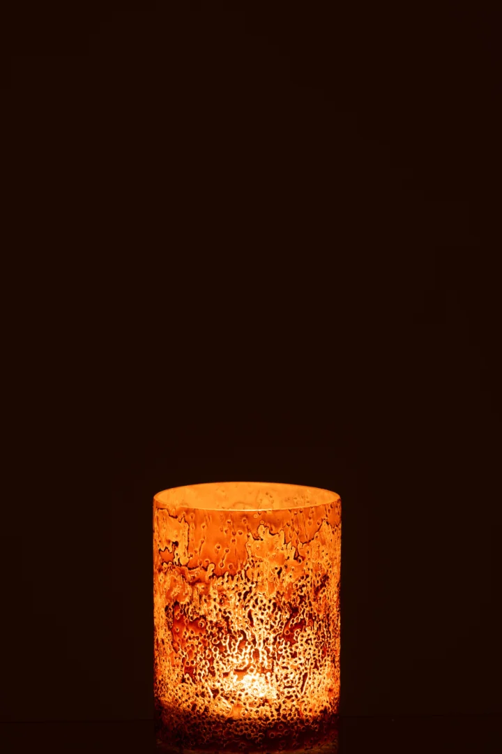 De Kaarsenhouder Orkaan Lijn Glas Roze Goud Klein, met zijn gestructureerde, gespikkelde roze-gouden glas, staat centraal tegen een donkere achtergrond en werpt een warme en uitnodigende gloed.