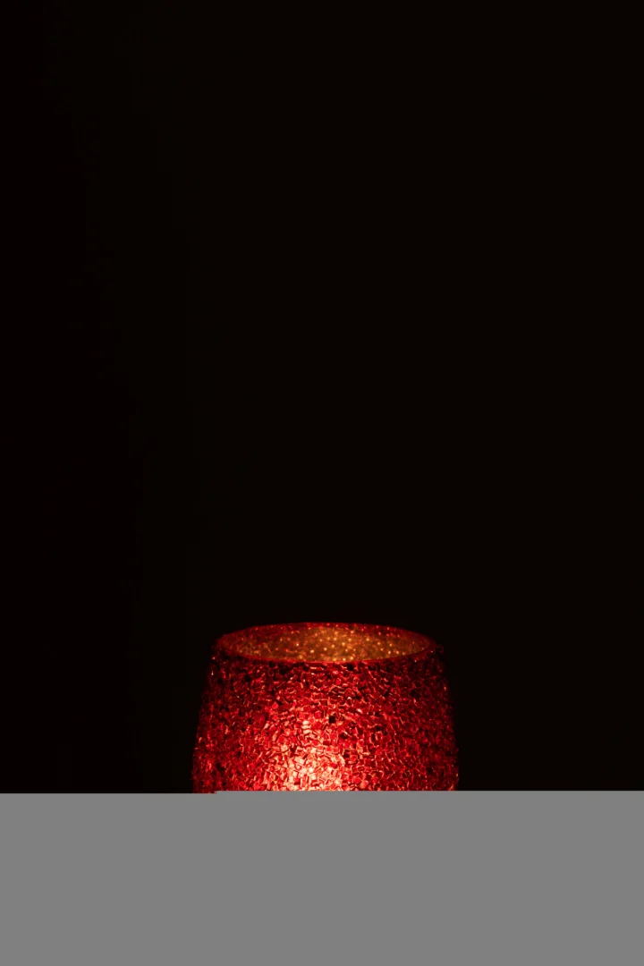 De Theelichthouder Glitter Glas Rood, met zijn rode glasstructuur, straalt warm in het onderste gedeelte van de afbeelding tegen een donkere achtergrond, waarbij alleen het bovenste gedeelte zichtbaar is.
