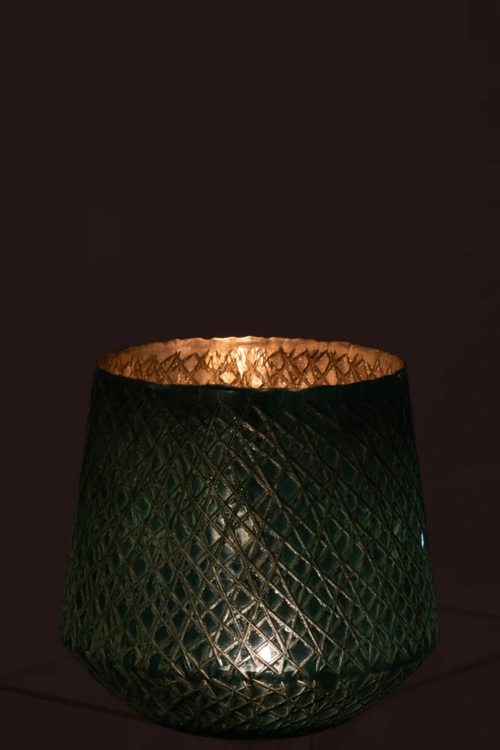 De Kaarsenhouder Orkaan Krassen Glas Mint Groen Groot heeft een decoratief patroon met textuur dat van binnenuit warm gloeit en een zacht gouden licht werpt tegen een donkere achtergrond.