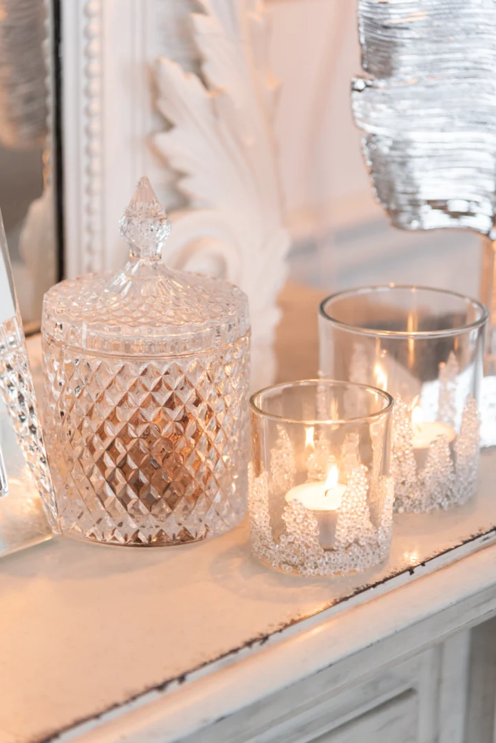 Een Theelichthouder Suikerbodem Glas Helder Middel staat op een wit vlak naast twee andere glazen kandelaars met brandende kaarsen, die het tafereel zacht verlichten en een vleugje warmte en elegantie toevoegen.