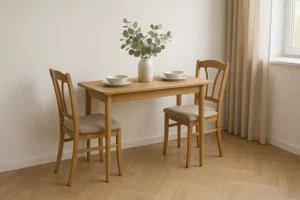 Een kleine houten eettafel - perfect als je je afvraagt "hoe ras is een smalle eettafel"- met twee bijpassende stoelen, gedekt met schalen en een vaas met groene bladertakken, staat bij een raam met beige gordijnen in een lichte, minimalistische kamer.