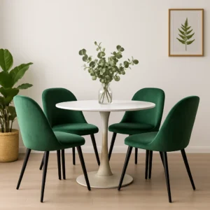 Een moderne eethoek met een ronde witte tafel en vier groene fluwelen stoelen laat zien hoe je 4 groene eetkamerstoelen combineert. Een vaas met groen, een potplant en een varenprint op de witte muur maken de minimalistische, frisse look compleet.
