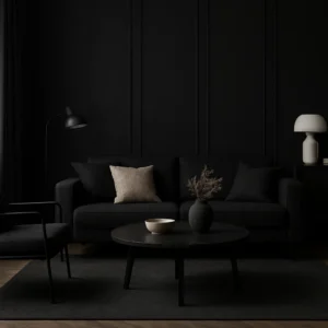 Een moderne woonkamer met donkere muren en meubels onderzoekt de vraag "Is zwart een goede interieurkleur?" met een zwarte bank met beige en zwarte kussens, een ronde salontafel, zwarte fauteuil, staande lamp en witte lamp op een bijzettafel.