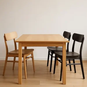 Een eenvoudige houten eettafel met twee zwarte stoelen rechts en een licht houten stoel links tegen een witte muur - de perfecte inspiratie als je je afvraagt: moeten stoelen lichter of donkerder zijn bij een houten tafel?.