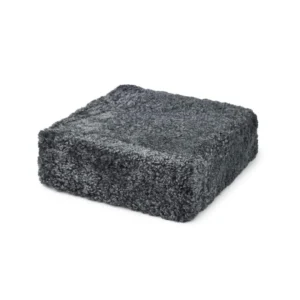 De Poef Schapenvacht Krullend Korte Wol M04 is een vierkant, donkergrijs pluche bed met een zacht, donzig oppervlak, afgebeeld op een witte achtergrond.