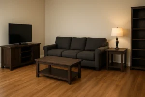 Een woonkamer met een donkergrijze bank, een houten salontafel, een tv op een houten standaard, een bijzettafel met lamp, een hoge boekenplank en een lichthouten vloer tegen beige muren - een inspiratie als je afvraagt: welke kleuren muren passen bij grijs en hout?.