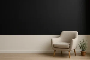 Een moderne, minimalistische woonkamer met een beige fauteuil en een kleine plant in pot op een lichte houten vloer, tegen een zwart-witte tweekleurige muur - perfecte inspiratie als je je afvraagt welke kleur zwart verzacht in een hedendaags interieur.