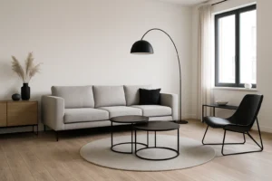 Minimalistische woonkamer met een lichtgrijze bank, zwarte staande lamp, ronde salontafels en een houten dressoir. Welke meubels zijn tijdloos? Neutrale kleuren, strakke lijnen en houten vloeren van hoge kwaliteit creëren een duurzame stijl voor elk seizoen.