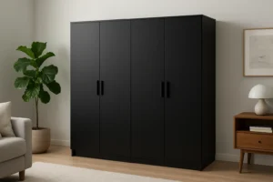 Een zwarte vierdeurs kledingkast met slanke handgrepen staat tegen een witte muur, naast een potplant en een houten nachtkastje met een lamp, en weerspiegelt waarom zwarte kasten in de mode zijn in deze moderne, minimalistische slaapkamer.