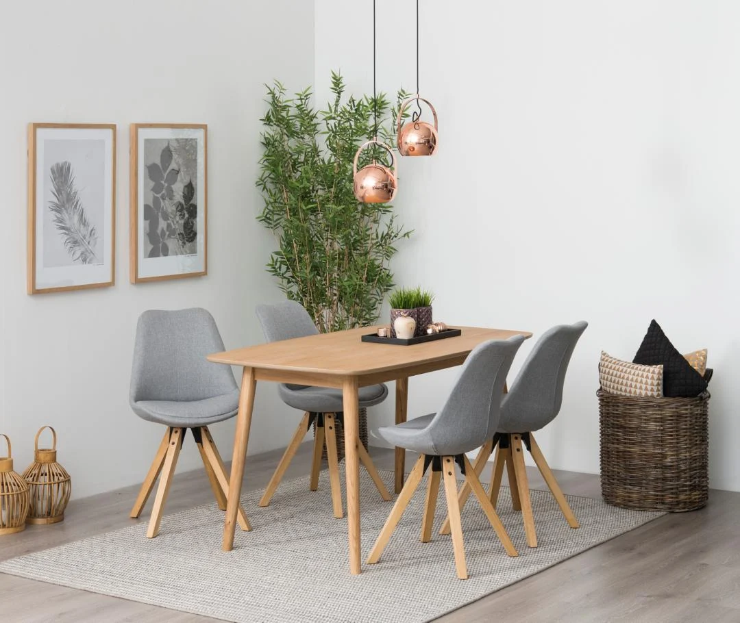In een moderne eetkamer staat de Eettafel Nieuwe Sfeer 150 x 80 CM Rond in eikenhout naturel, gecombineerd met vier grijs gestoffeerde stoelen, hanglampen, een bladplant, ingelijste muurkunst en een gezellige mand met kussens.