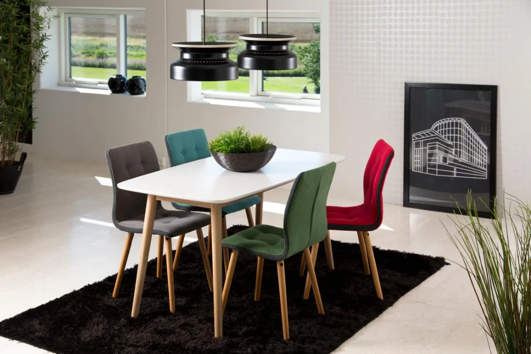 Een moderne eetkamer met de Eettafel Nieuwe Sfeer 150 x 80 CM (rechthoek eikenhout), vijf kleurrijke stoelen (groen, rood, donkergrijs), een zwart vloerkleed, zwarte hanglampen, potplanten en een ingelijste architectuurprint tegen de muur.