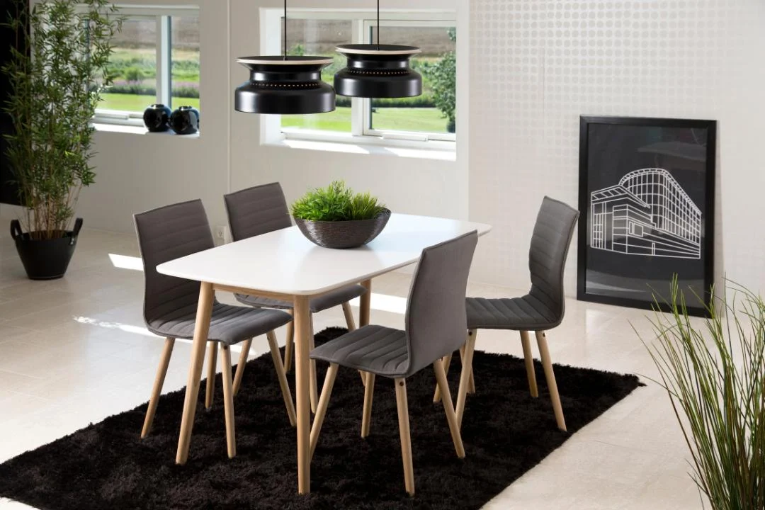 Een moderne eetkamer met de Eettafel Nieuwe Sfeer 150 x 80 CM rechthoek eikenhout tafel, vier grijze stoelen, een zwart vloerkleed, twee zwarte hanglampen, een plantenpot, grote ramen en ingelijste kunstwerken aan de muur.