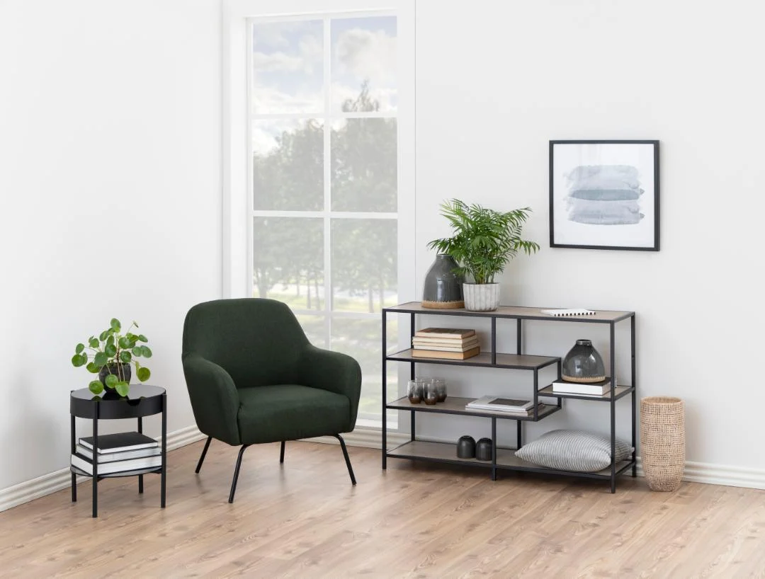 Interieur met zwarte stalen boekenkast en groene fauteuil. De asymmetrische kast heeft sonoma eiken planken. Lichte houten vloer.