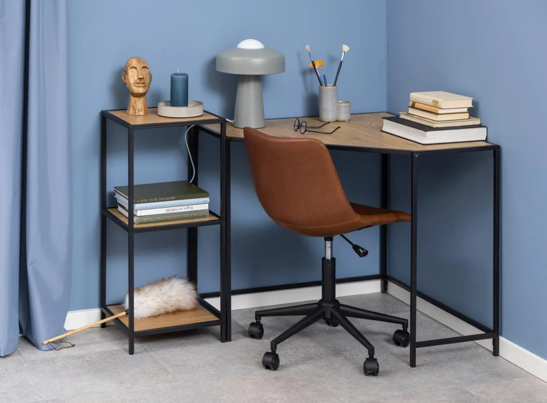 Een modern kantoor aan huis met een bruine draaistoel aan een hoekbureau, gedecoreerd met boeken, een lamp, een kaars, een houten beeldhouwwerk en een bril. Aan de blauwe muren hangt een Seaford boekenkast met nog meer boeken en een plumeau.