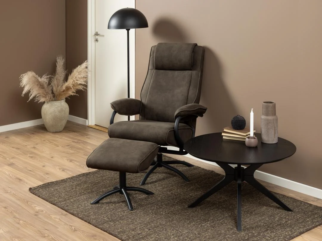 Een moderne woonkamer met de Salontafel Zwart 80 CM Rond Eikenfineer als zwarte ronde bijzettafel, met een bruine relaxfauteuil en voetensteun, staande lamp, grote vaas met gedroogd gras en een lichthouten vloer.