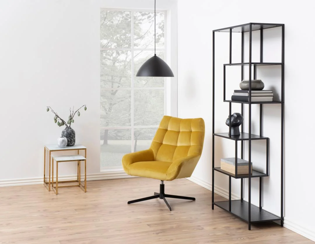 Een moderne minimalistische kamer met een gele fauteuil, een Seaford boekenkast met decoratieve items, kleine bijzettafeltjes met een vaas en een groot raam dat natuurlijk licht binnenlaat.