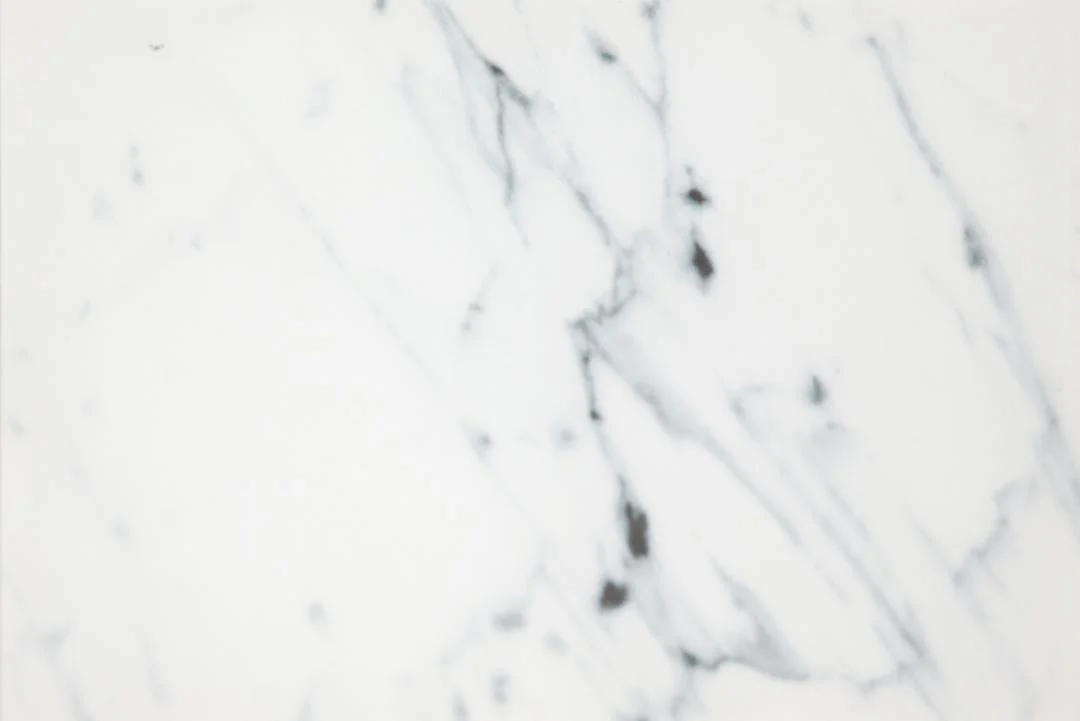 De Salontafel Goud, Wit 80 CM Rond Kunststof heeft een wit marmerachtig oppervlak met zachtgrijze en zwarte diagonale aderen, waardoor een glad en natuurlijk steenachtig patroon ontstaat.