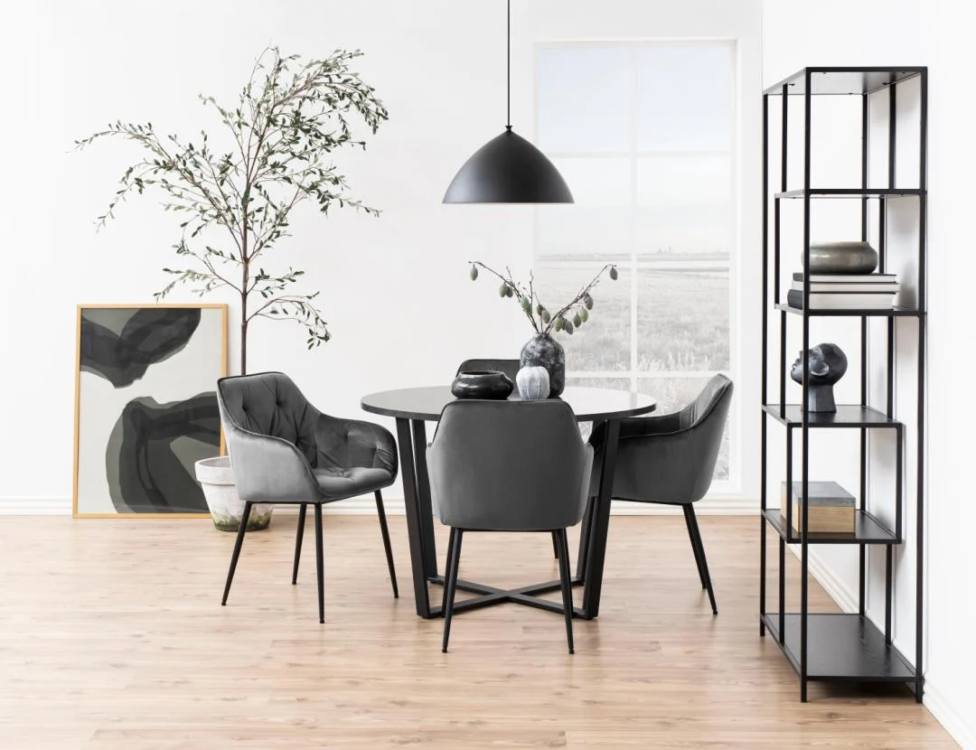 Een moderne eetkamer met de Eettafel Amble Rond Marmer Metaal Mat met zwart onderstel, drie grijze stoelen, een zwarte hanglamp, een metalen plank met decor, een potplant en abstracte kunst tegen een witte muur en groot raam.