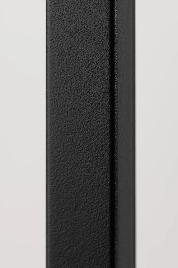 Detailopname van een zwart stalen frame, mogelijke boekenkast. De textuur is korrelig en het licht is zacht, tegen een witte achtergrond.